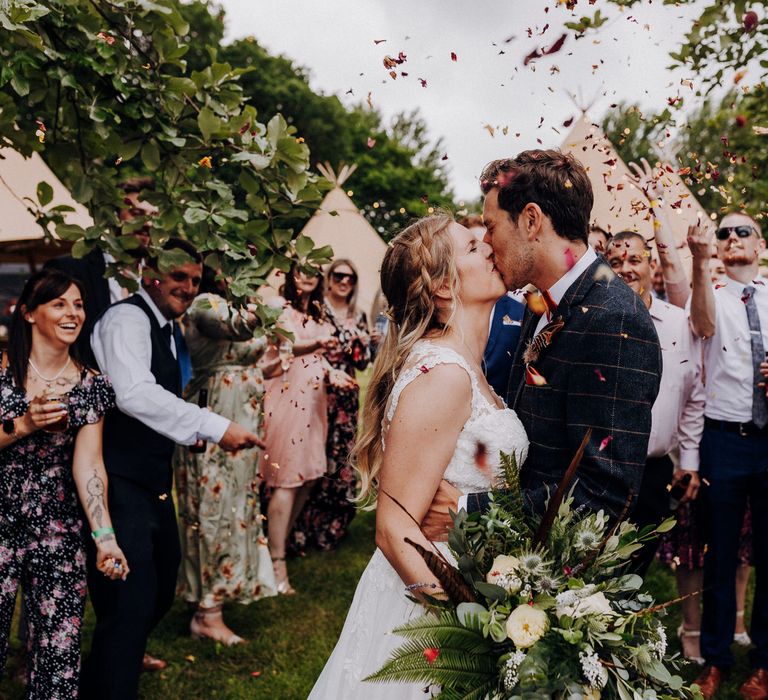 Bride & groom kiss in the middle of wedding party as they throw confetti around them