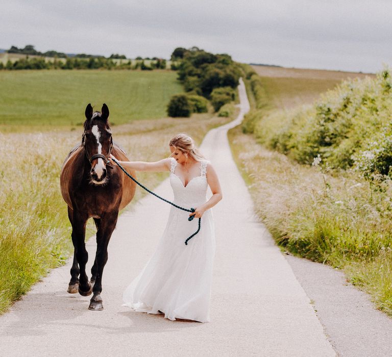 Bride walks with her horse through countryside on her wedding day