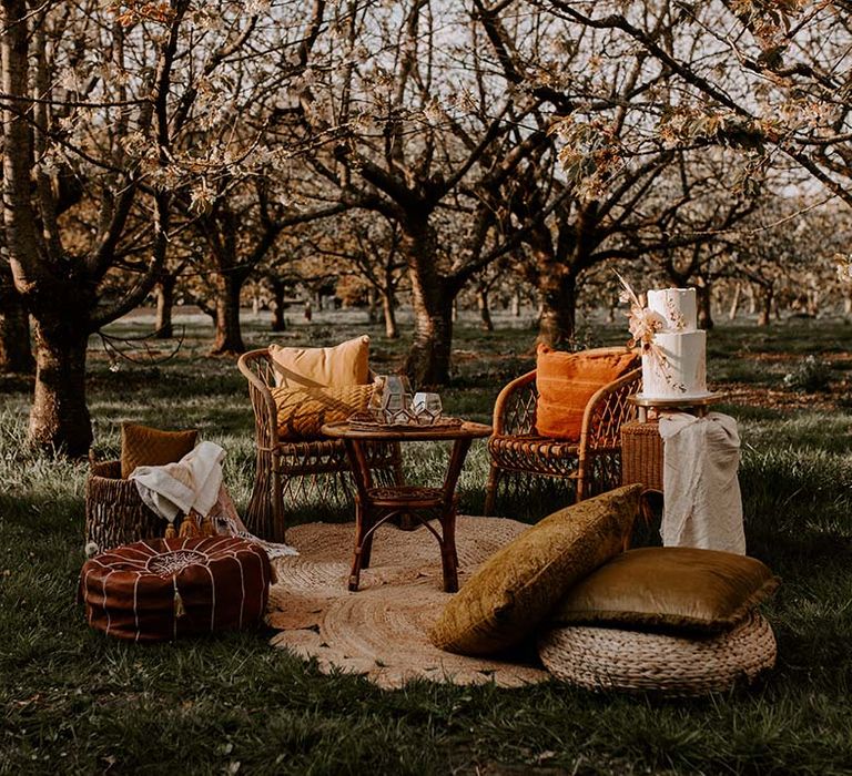 Outdoor chill out area with wicker chairs, pouffe and buttercream wedding cake 