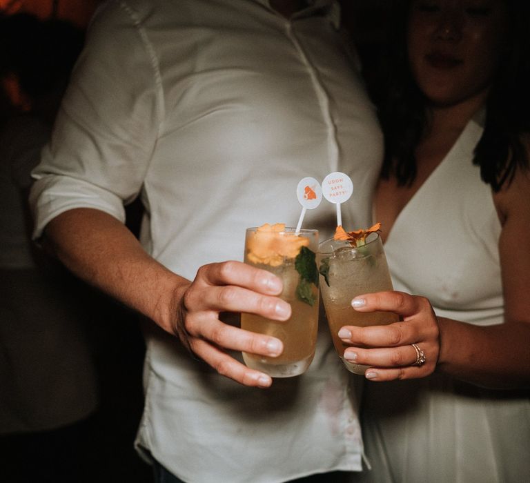 Bride and groom drinking signature orange cocktails with stirrers 