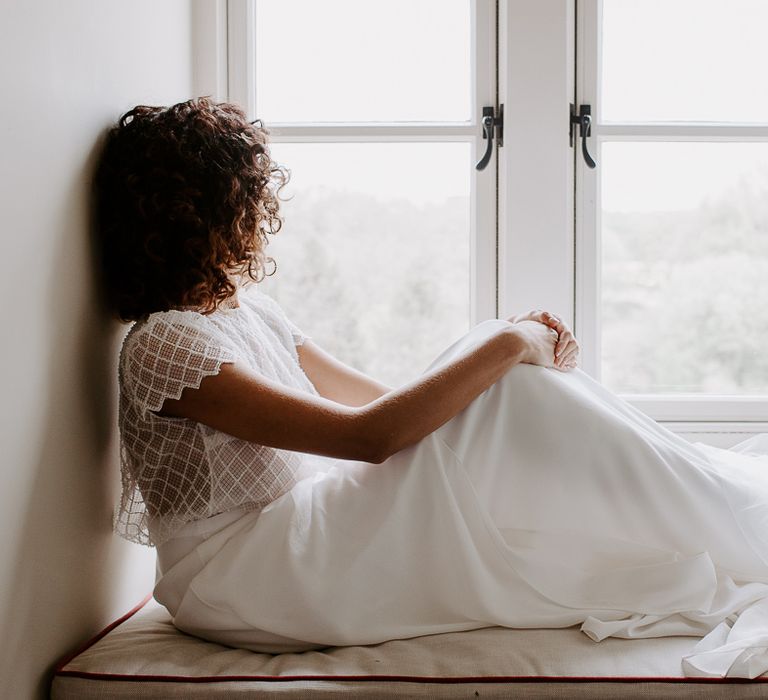 Bride with naturally curly hair sitting on a window sill in bridal separates with sequin top 