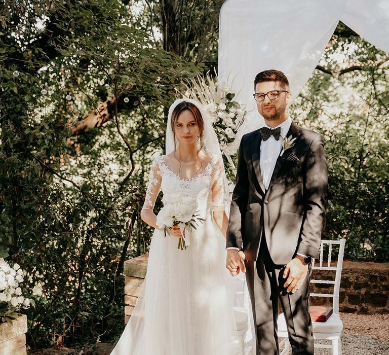 Bride & groom stand together after their wedding ceremony outdoors as groom wears black tie | Royal Studio