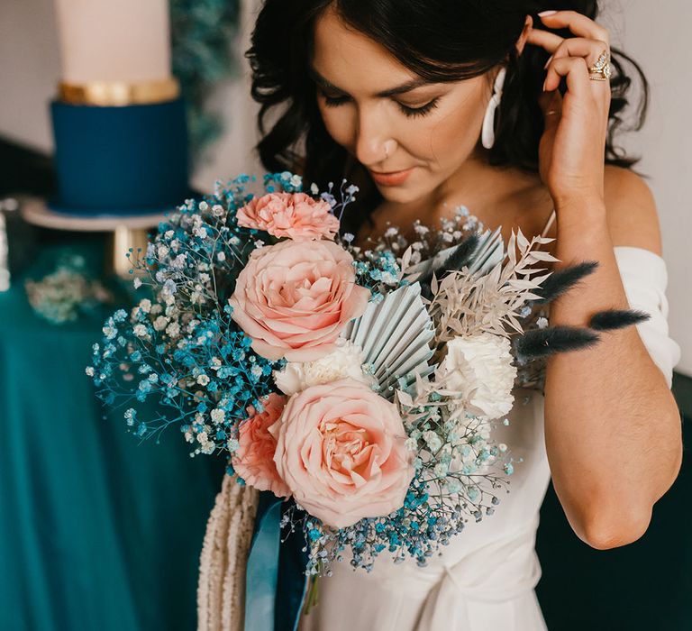 Bride with wishbone rings on tucking her wavy hair behind her ear holding her pink rose and teal gypsophila wedding bouquet 