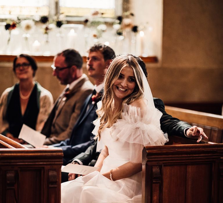 Bride in white Halfpenny London Mayfair dress sits in pew during church wedding ceremony in Cornwall