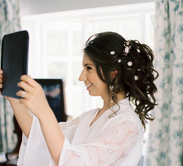 Bride looks at her hair on the morning of her wedding day whilst wearing white dressing gown