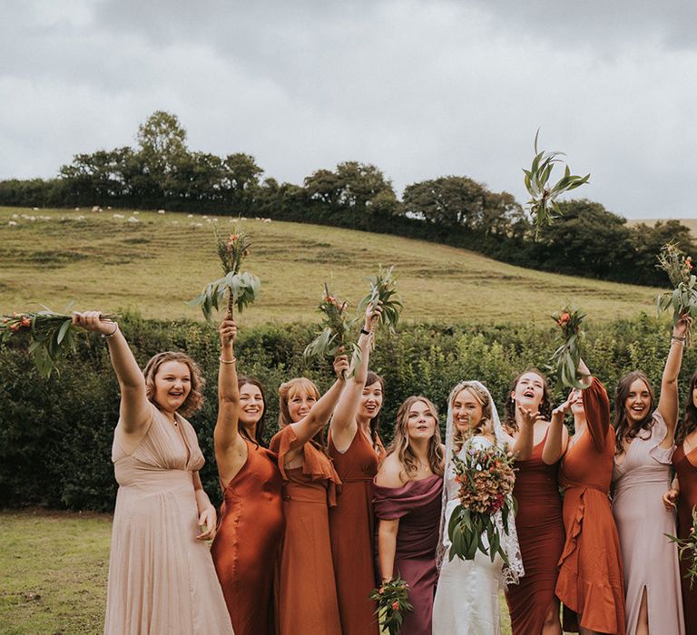 Bride stands with her bridesmaids who wear Autumnal coloured bridesmaids dresses in differing styles