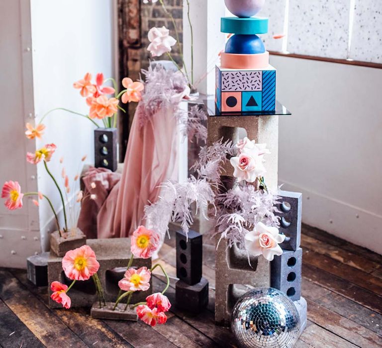 Industrial wedding display with concrete plinths, drapes, disco balls, flower stems and a monumental wedding cake 