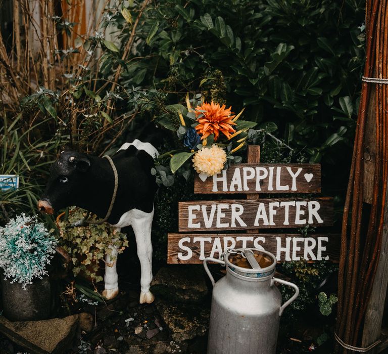 Large floral bouquet by wooden sign reading 'Happily Ever After Starts Here' and milk churn at The Wellbeing Farm for wedding