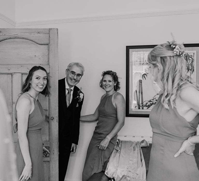 Father of the bride in dark suit and buttonhole smiles as he sees bride for the first time before church wedding ceremony