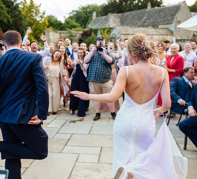 Bride in a beaded wedding dress and trainers and groom in a navy suit and trainers perform a surprise first dance outside at their Caswell House wedding 