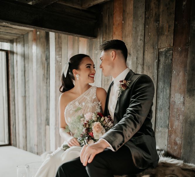 Bride & groom sit with one another in front of wooden backdrop