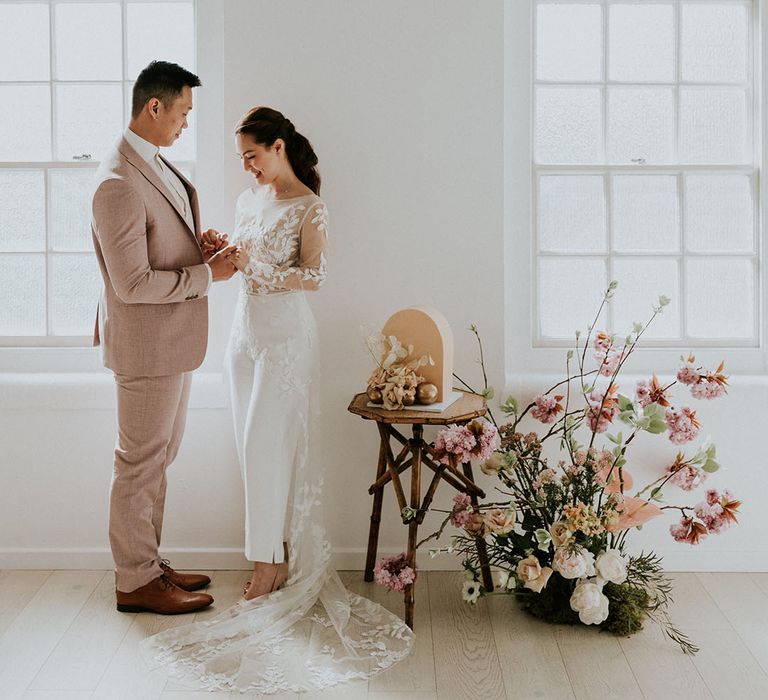 Asian bride in a jumpsuit and groom in a beige suit hold hands at their minimalist wedding with asian wedding decor  