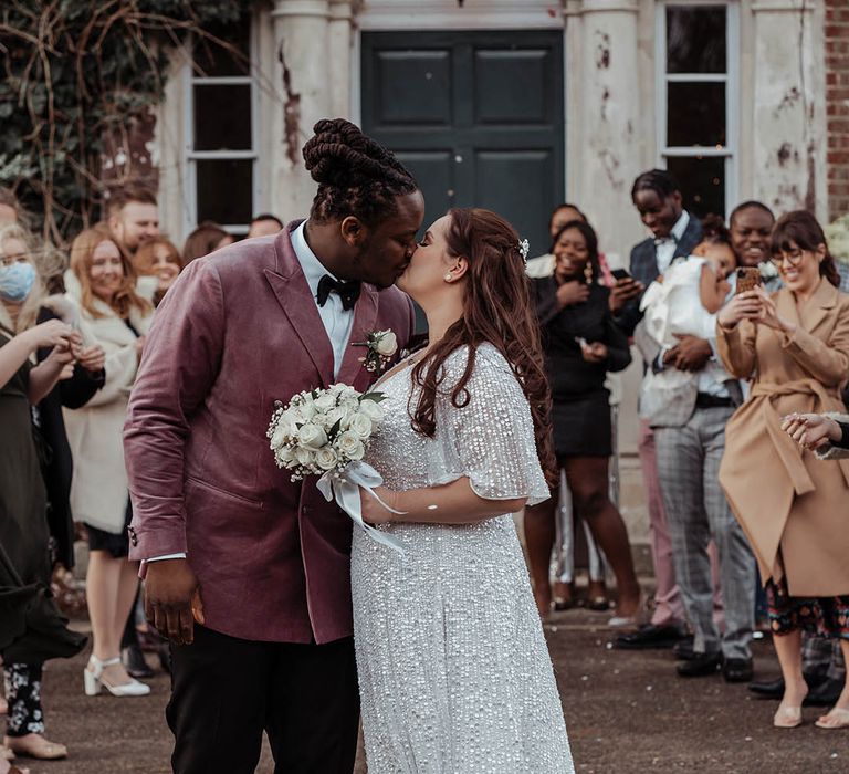 Bride & groom leave ceremony as wedding guests throw confetti around them and they kiss 