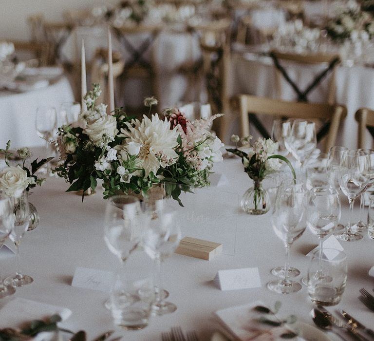 White and neutral table setting with acrylic table number sign on wooden stand with small flower arrangement