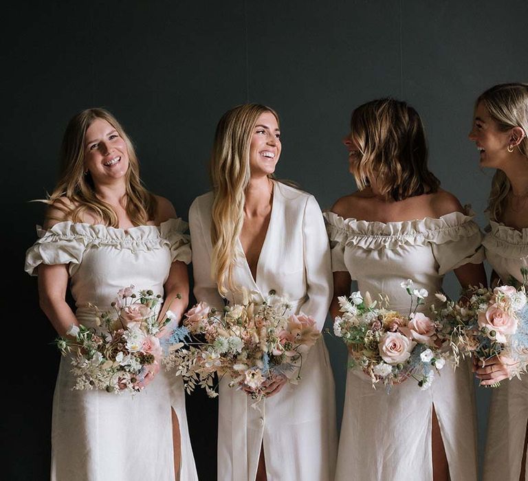 Bride with long blonde hair with bridesmaids in off the shoulder off-white dresses with pastel summer bouquets