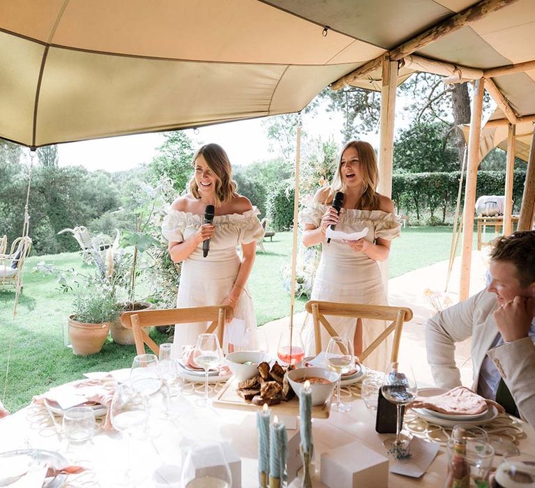 Bridesmaids in off the shoulder white dresses give their wedding speeches at circular tables inside the Buffalo Tipi