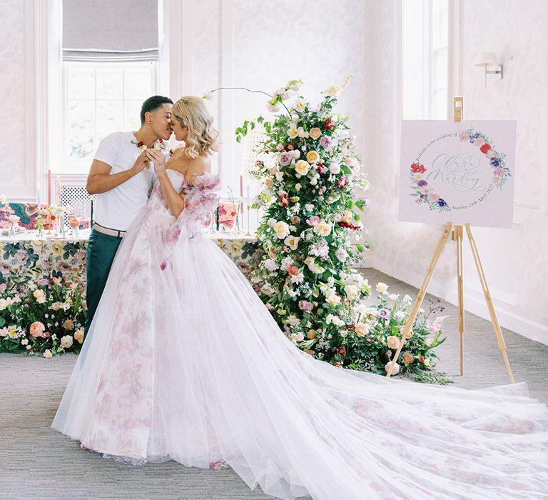 LGBTQI+ couple kissing in the reception room with floral table cloth, flower arrangements and wedding welcome sign 