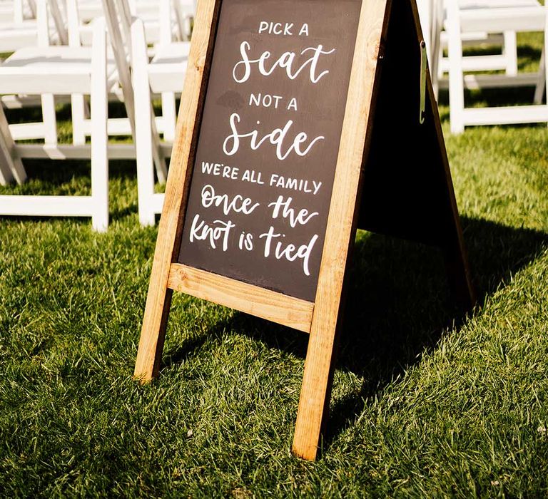 Chalk board wedding welcome sign directing guests to their white wooden seats 