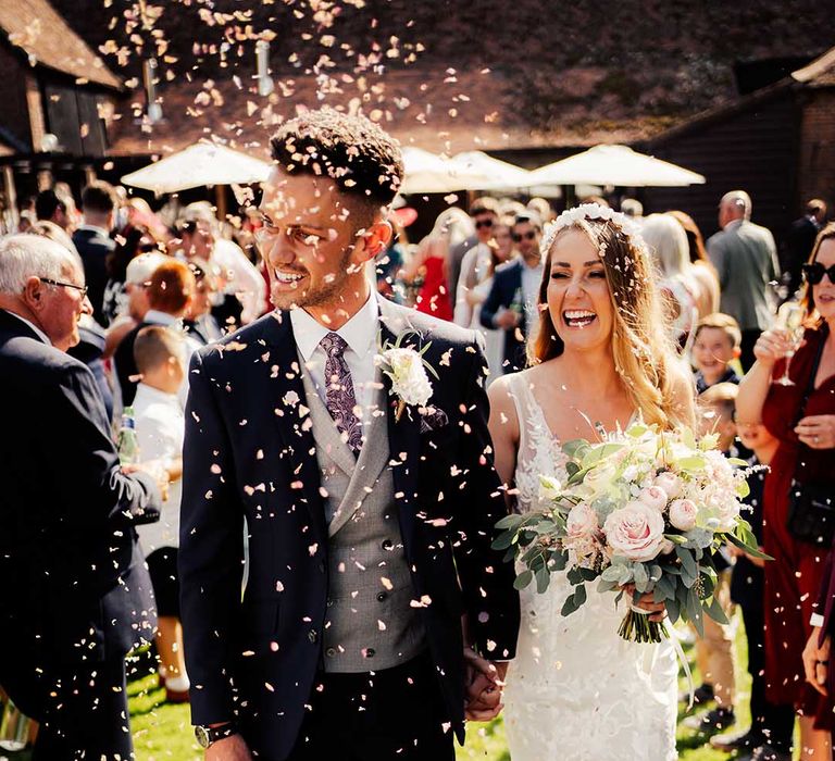 Bride and groom smile together as they walk through white confetti thrown for them