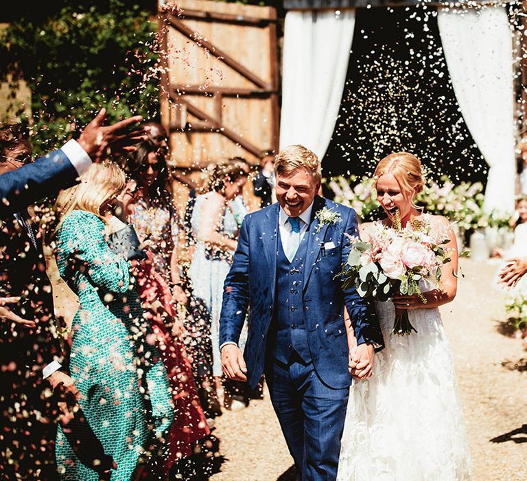 Bride and groom happily exit their wedding ceremony as husband and wife to white confetti being thrown 