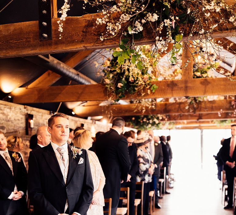 Groom in three piece morning suit looks nervous as he stands at the altar waiting for the bride at Dewsall Court wedding