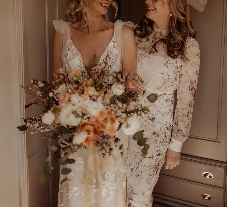 Bride carrying autumnal wedding bouquet with her mother wearing a fascinator and floral pattern dress 