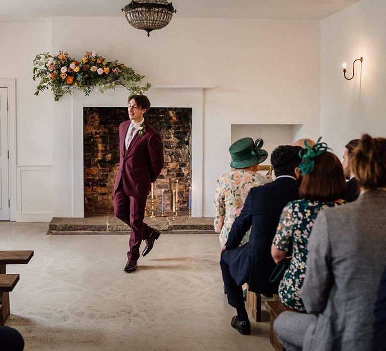 Groom in three piece burgundy suit waits nervously at the altar for the bride on their wedding day at Aswarby Rectory