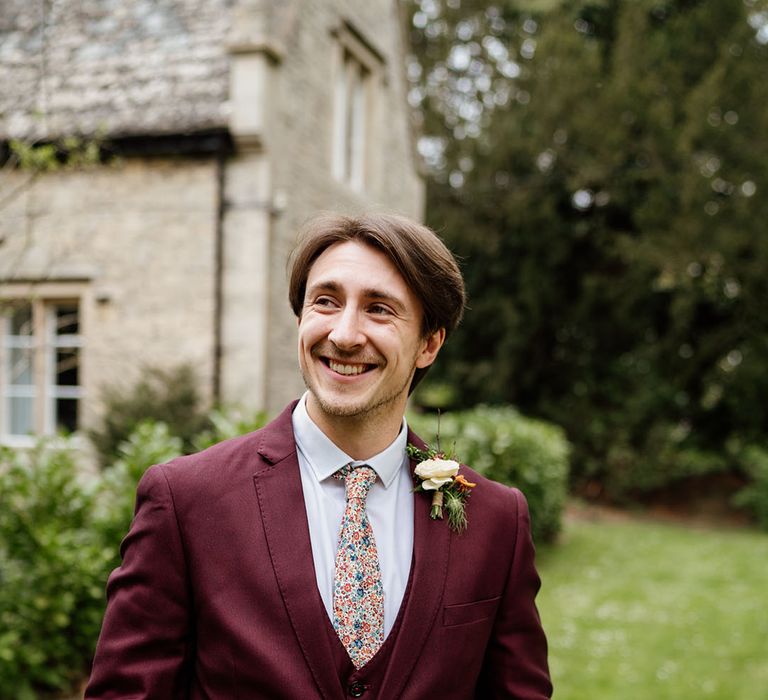 Groom in three piece burgundy suit with patterned tie and white shirt 