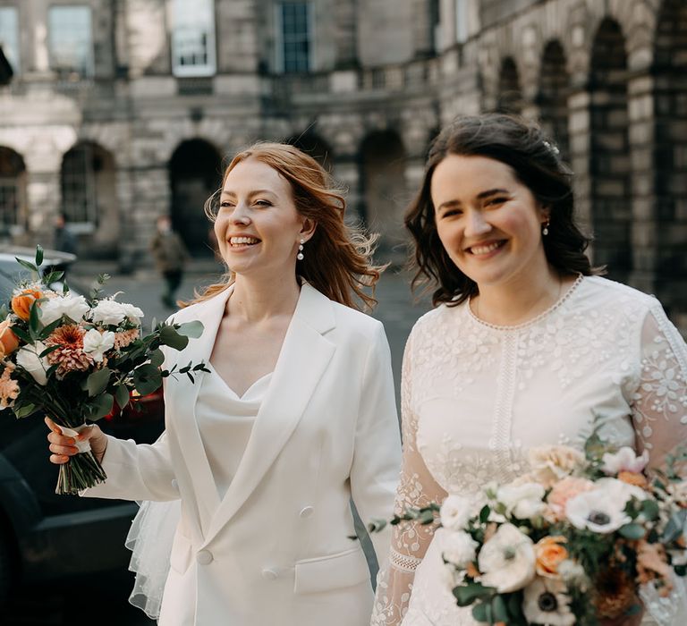 Brides walk alongside one another in bridal suit and boho wedding gown