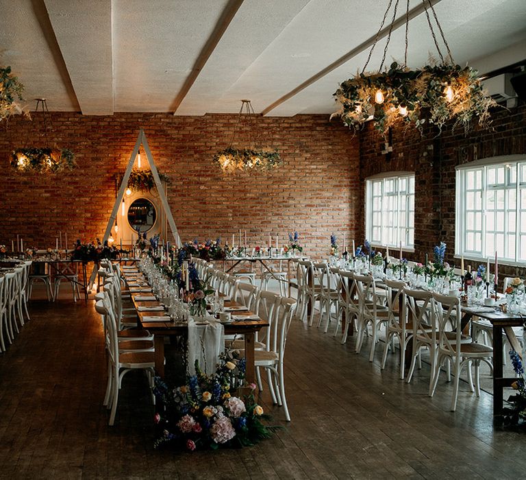 Exposed lightbulb chandeliers with foliage hang in Larkspur Lodge with pastel table setting styled with wildflowers