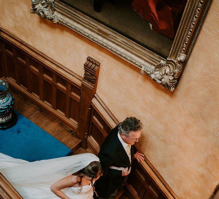 Bride walks down staircase whilst veil trails behind her 