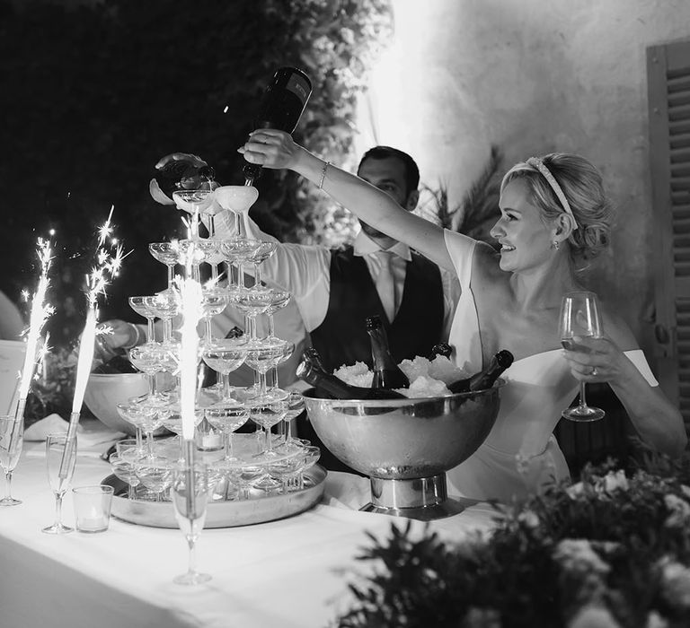 Bride pours champagne into glasses for champagne tower