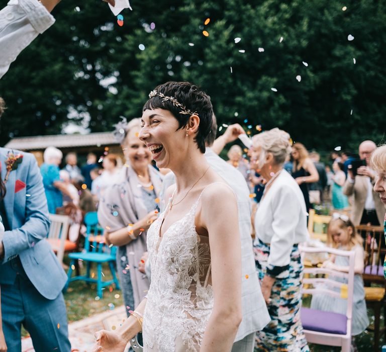 Bride wears lace Enzoani wedding dress as brightly coloured confetti is throw around her