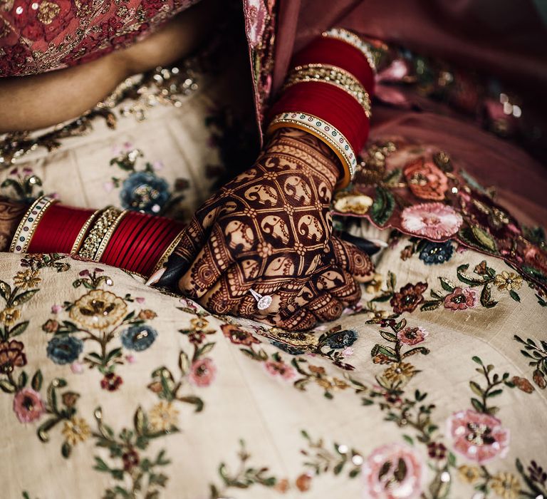 Bride wears traditional mehndi with elephant design and wears red and gold bangles 