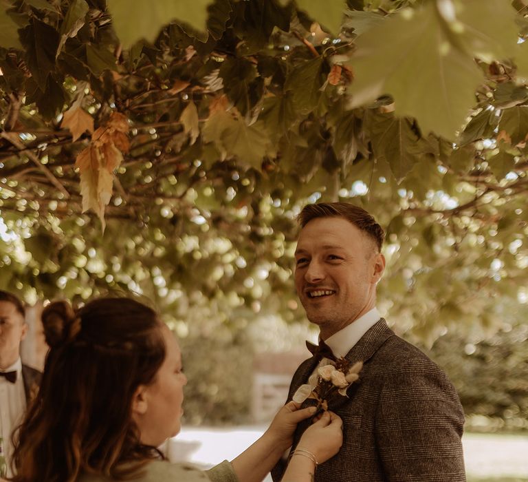 Wedding guest helps a groomsman put on his bunny grass dried grass buttonhole 