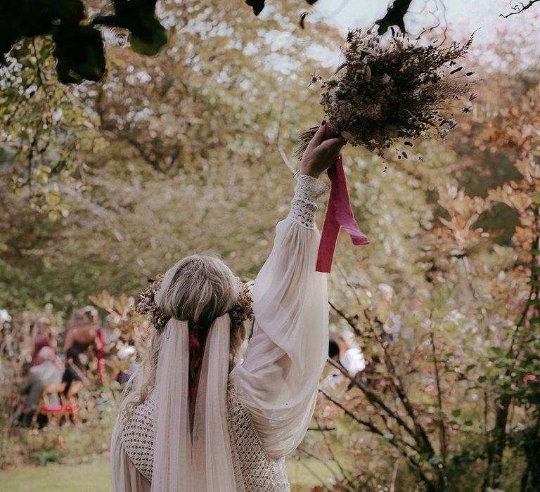 Bride lifts dried floral bouquet in the air tied with red ribbon 