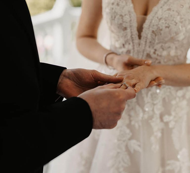 Groom in a black three piece suit puts on the bride's wedding ring 