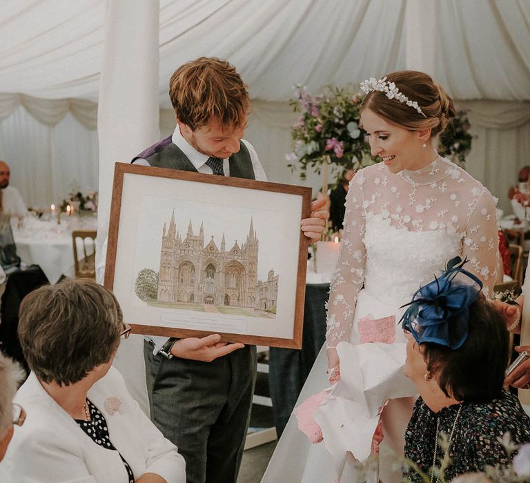 Bride and groom open up a wedding present painting of the cathedral they just married in 