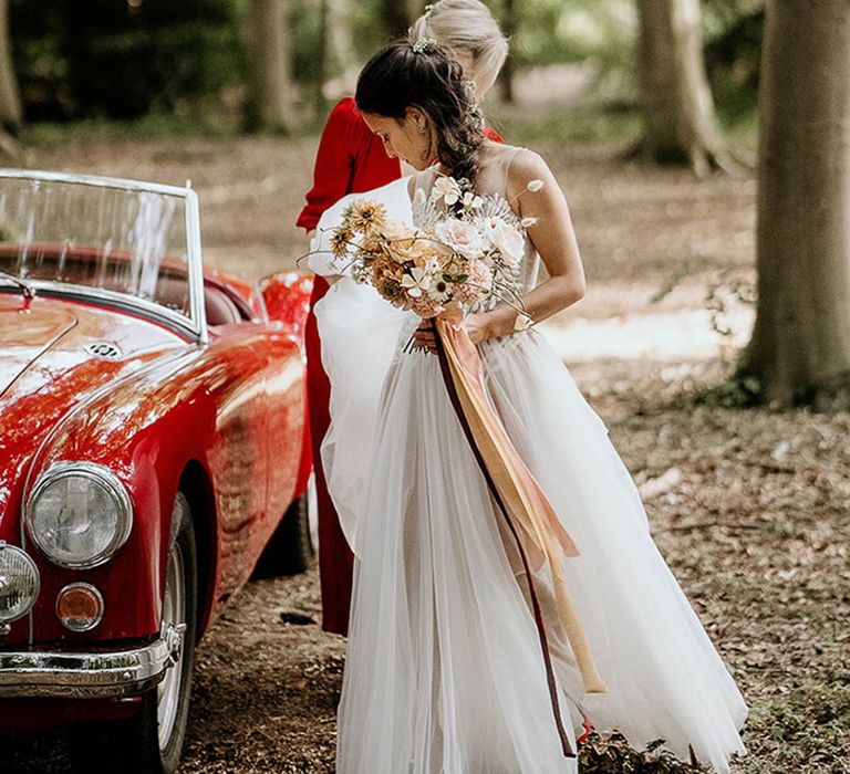 Bride and bridesmaid in magenta dress exit the bright red wedding car 