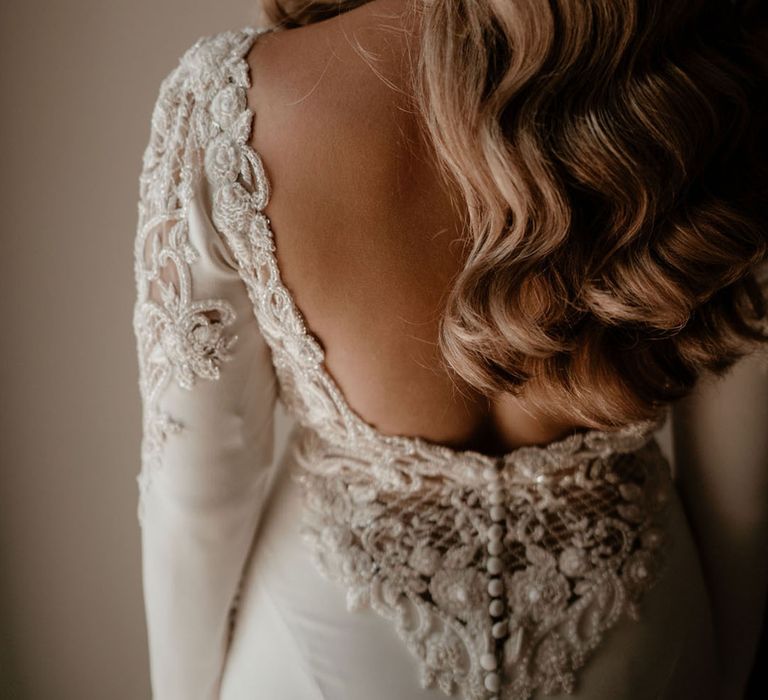 Bride in a low back Badgley Mischka wedding dress with lace beaded and button detail and curled blonde hair 