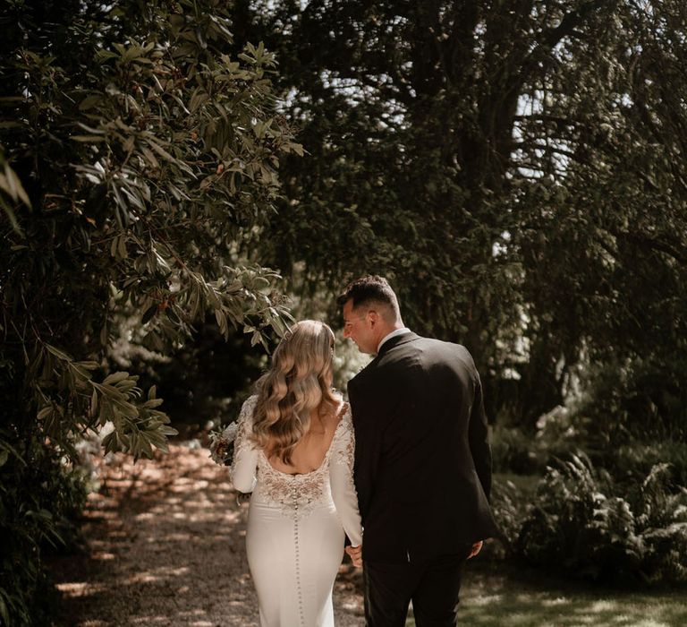 Bride in a button back wedding dress with lots of lace and beading details walking holding hands with the groom 