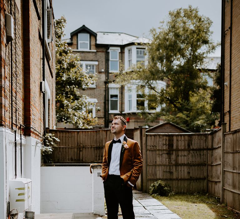 Groom shows off alternative wedding suit featuring a burnt orange velvet blazer