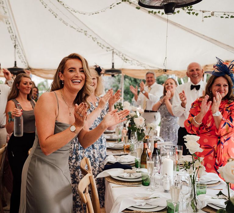 The wedding guests stand and applaud as the bride and groom arrive in for their reception at Pythouse Kitchen Gardens