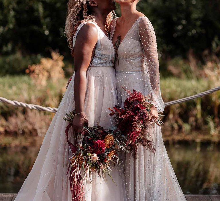 Bride in golden leaf crown and sleeveless peach gown with star embroidery laughing with bride in crystal embellished gown and gold headdress 