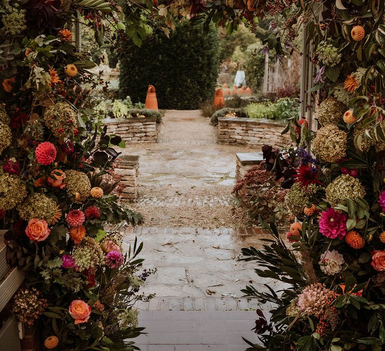 Large luxe floral arch with white and pink carnations, garden roses, red strawflower, eucalyptus, baby’s-breath and various dried flowers  