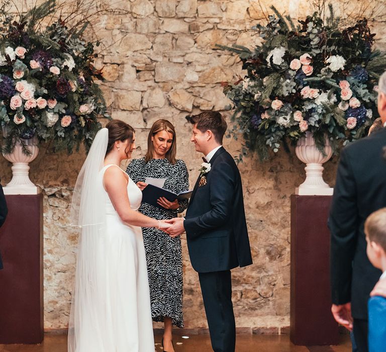 Bride and groom stand opposite each other holding hands for their civil wedding ceremony at Notley Abbey 