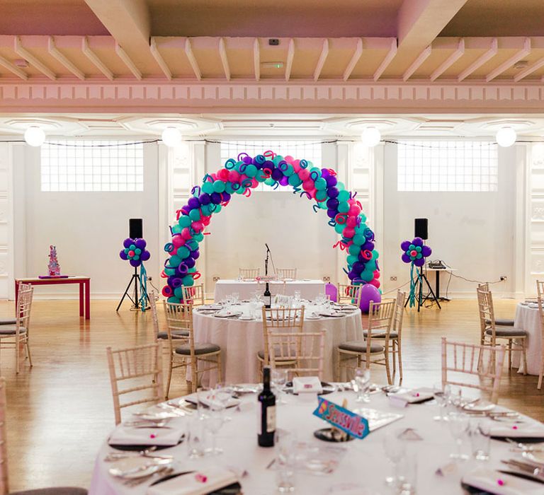 Reception room of theme park wedding at Margate Dreamland with blue, pink and purple balloon arches and columns, large speakers and a neutral tablescape theme 