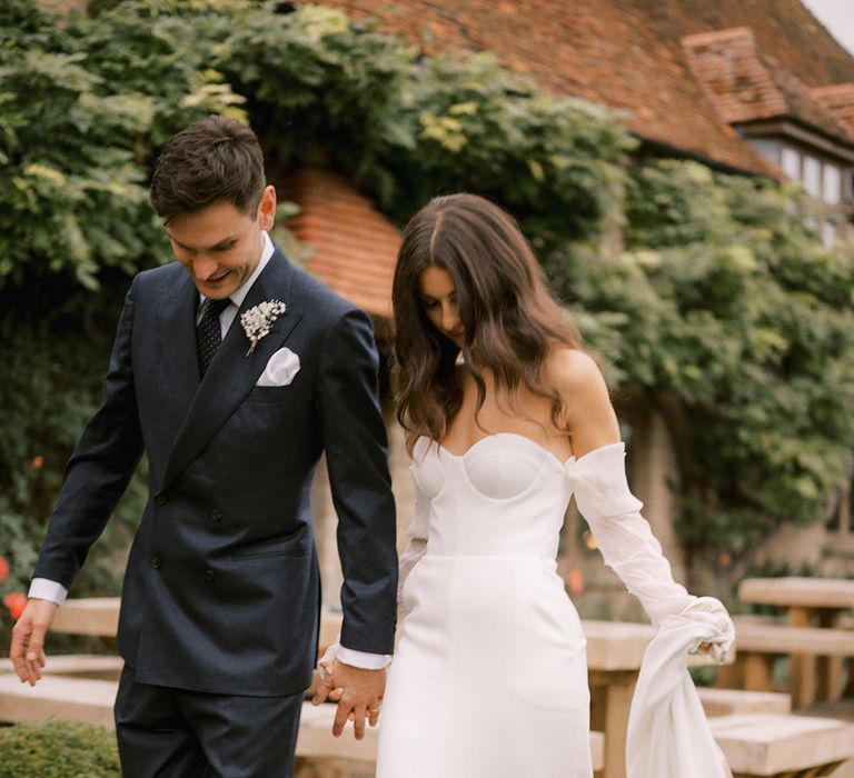 The bride walks in her platform Jimmy Choo pearl shoes in a modern strapless wedding dress with the groom in a navy suit 