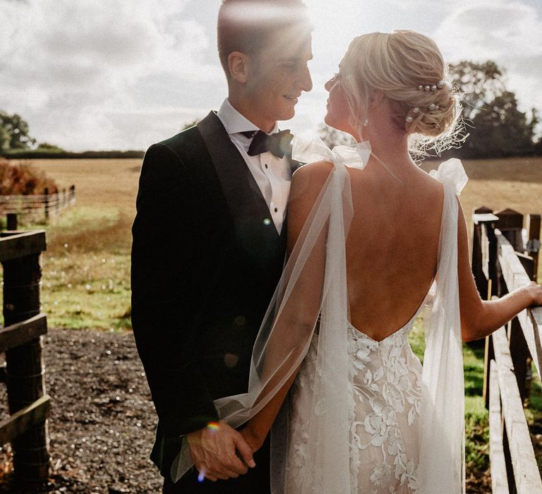 Bride in fitted lace Made With Love wedding dress with pearl hair pin accessories standing during golden hour with the groom 