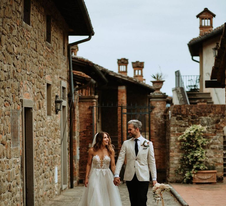 Bride in white embroidered tulle wedding dress with groom in linen suit walking through Italian villa at destination wedding